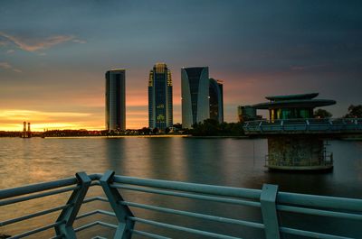 Sea by modern buildings against sky during sunset