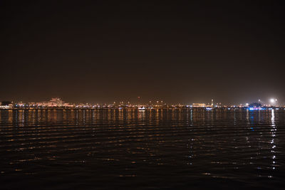 Illuminated city by sea against clear sky at night