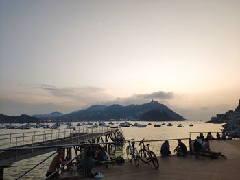 People on shore against sky during sunset