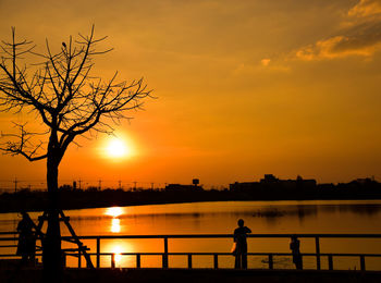 Silhouette man standing by river against sky during sunset