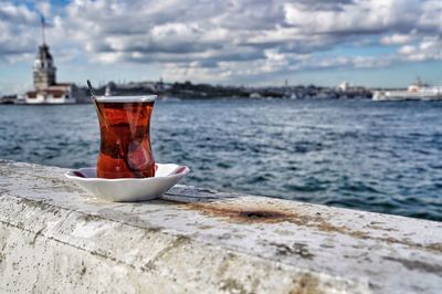 Close-up of turkish tea by sea against cloudy sky