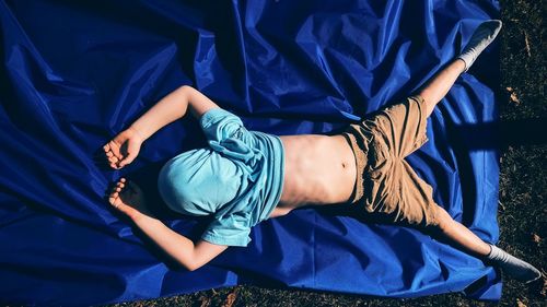 Full length of boy with covered face sleeping on blue fabric in yard