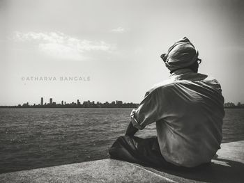 Rear view of man sitting by lake against sky