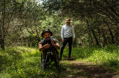 Photographers with hats taking photos with camara tripoid front view on woodland over  grass  