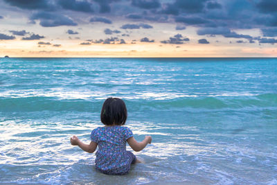 Rear view of girl sitting at beach against sky