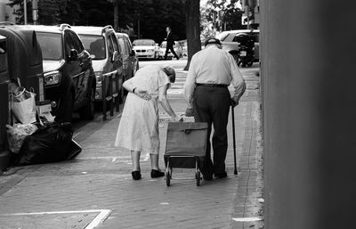 Rear view of senior couple with luggage walking on footpath