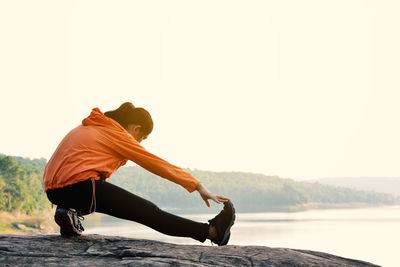 Full length of woman stretching on rock formation against clear sky