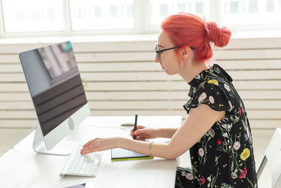 Side view of woman using phone while sitting on table