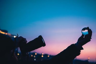 Person photographing while holding crystal ball against sky during sunset