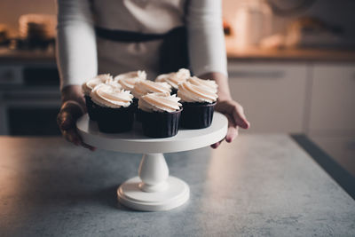 Woman baked tasty chocolate cupcakes with whiped cream cheese staying on table in kithen closeup.