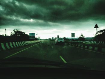 Cars moving on road against cloudy sky