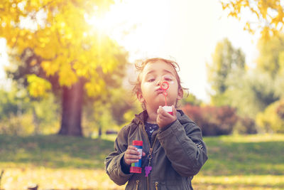 Smiling girl blowing bubbles while standing on field