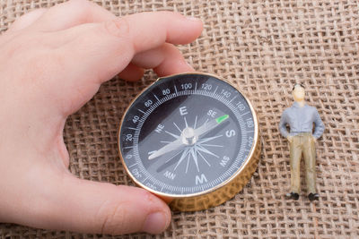 Close-up of hand holding navigational compass by figurine on jute