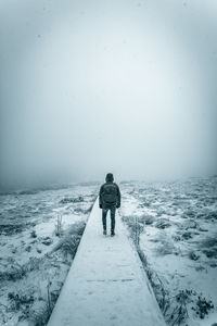 Rear view of man walking on snow covered land against clear sky