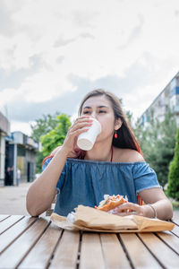 Hungry stylish woman, enjoying eating a burger outdoors, dressed in jeans shirt, wearing sunglasses