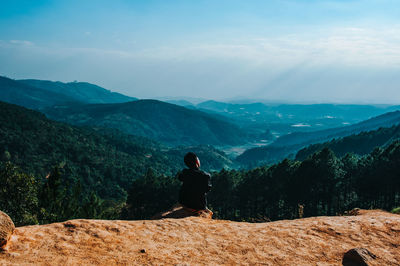 Rear view of man sitting on mountain against sky