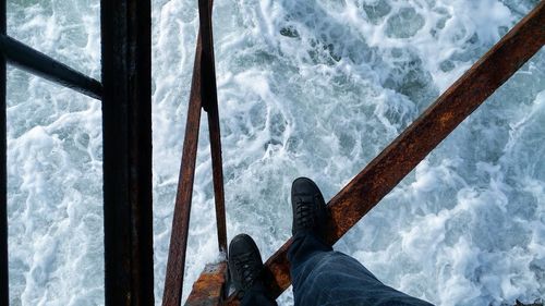 Low section of man standing on railing over sea