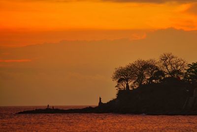 Silhouette tree by sea against orange sky