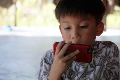 Boy looking away while using mobile phone outdoors