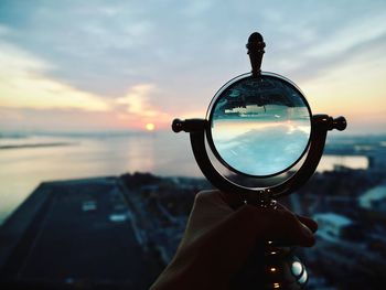 Person holding sunglasses against sky during sunset