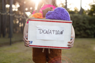 Midsection of girl holding box with donation text while standing outdoors