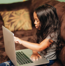 Mixed race young girl at home on the sofa using a laptop computer for learning