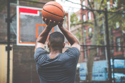 Rear view of young man practicing basketball in court