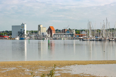 Sailboats moored at harbor against sky in city