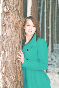 Portrait of smiling young woman standing against tree trunk