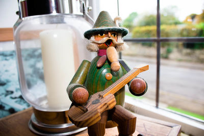 Close-up of wooden figurine by lantern against window