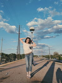 Full length of woman with hands behind head standing on street against sky