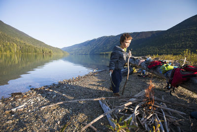 Young boy carries sticks to add to lakeside fire during a camping trip