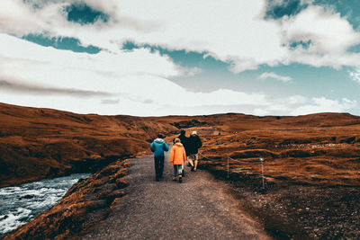 Rear view of people walking on mountain against sky