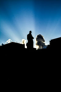 Low angle view of silhouette statue against blue sky