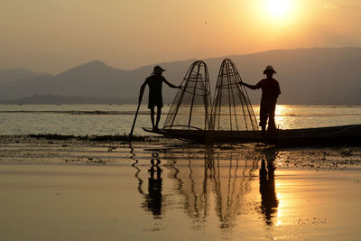 Silhouette men fishing in lake at sunset