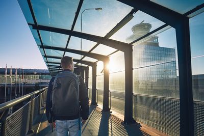 Rear view of man with backpack standing in city during sunset