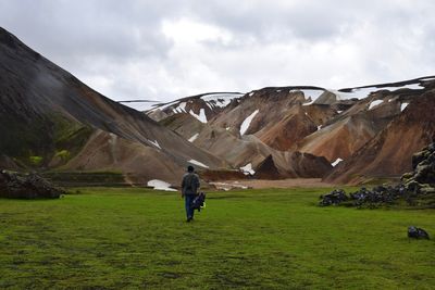 Rear view of men walking on field against sky