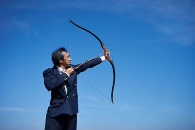 Businessman with bow and arrow on field against sky