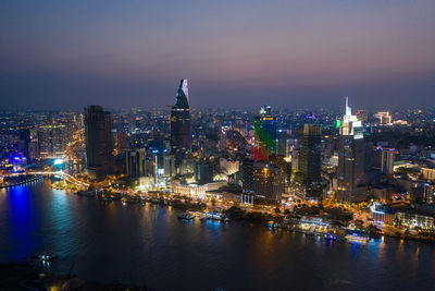 Illuminated buildings by river against sky in city at night