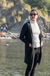 Fashionable young woman standing against lake and mountain