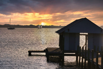 Silhouette house by sea against orange sky