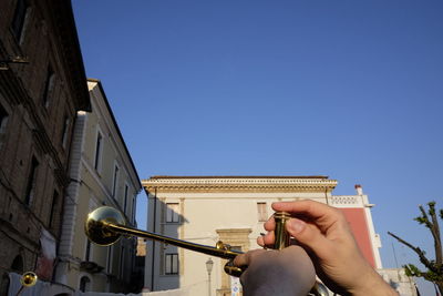 Cropped hands of man playing trumpet against clear blue sky