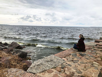 Woman sitting on rock by sea against sky