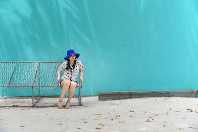 Full length of woman sitting against blue wall