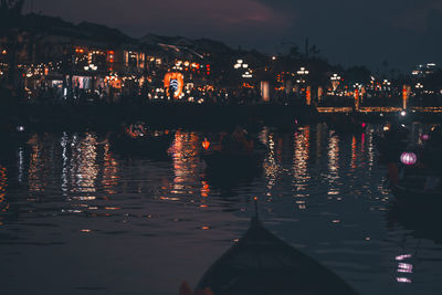 Illuminated city by lake against sky at night