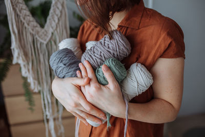 A young brunette girl in a brown shirt at home holds multi-colored threads for macrame in her hands