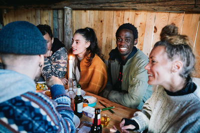 Portrait of young man sitting with friends talking while having food in log cabin