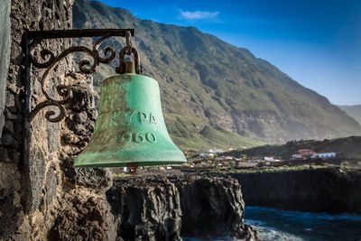 Old rusty bell hanging from wall against mountain range