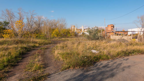 Road amidst field and buildings against sky