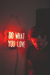 Man looking down while standing by illuminated text on wall